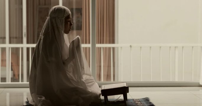Muslim woman praying to the GOD while wearing veil after reading Quran at home. Shot in 4k resolution