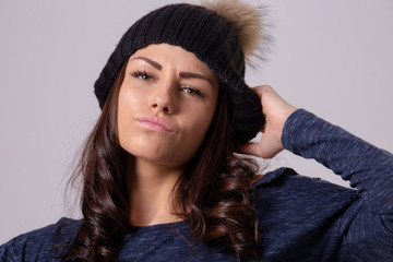 Portrait of attractive brunette woman wearing warm hat and pullover posing on light background