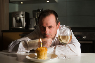 Sad old man sitting at table, celebrating a birthday alone and sad looking at a cupcake.