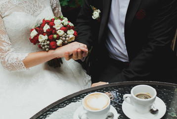Wedding couple is sitting near the glass table and drinking coffee. Bride in lace satin dress is...