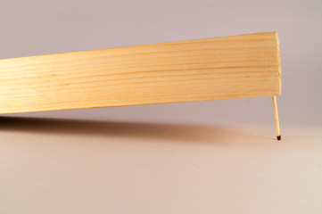 A thick wooden bar, located obliquely, is held by a thin match.
