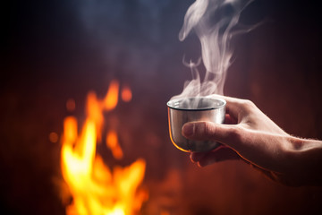 Hand holding cup of hot tea by the fire