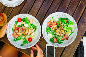 salad with vegetables and bacon with rubbed cheese. on the table near the plate the phone and hands of the girl