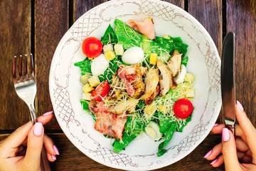A plate of caesar salad with fresh vegetables, quail eggs, cherry tomatoes and grilled chicken and bacon.