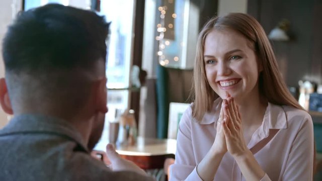 Medium shot of happy young woman laughing while listening to man talk during first date in restaurant