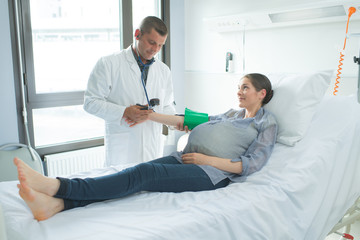 Obraz premium male doctor checking pregnant woman blood pressure in hospital