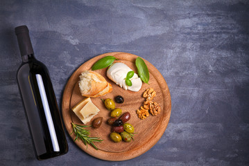 Bottle and glass of wine with cheese, olives, bread, nuts and basil on dark background. Wine and food concept. View from above, top