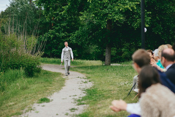 Fototapeta premium Groom in the stylish wedding suit going to the bride with a bouquet of flowers. Back view