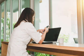 Beautiful woman using smartphone searching information and laptop