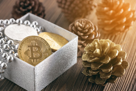 Golden bitcoin placed in silver glitting gift box with pine cone on wooden table