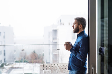 A man by the window holding a cup of coffee at home.