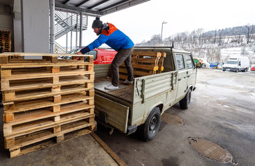 Man is loading wooden pallets on a truck in winter. Stacking wooden euro pallets on a truck lorry...