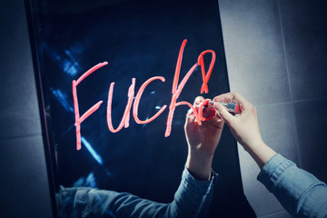 Woman writing "fuck" on a mirror with a red lipstick.