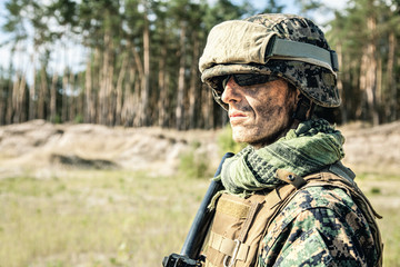 Location shot of United States Marine with rifle weapons in uniforms. Military equipment, army helmet, warpaint, smoked dirty face, tactical gloves. Weapons, army, american pride, patriotism concept - obrazy, fototapety, plakaty