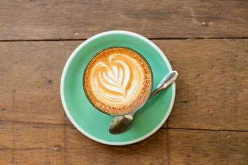 Top view of a cup of piccolo latte hot coffee on a green saucer with latte art and on wooden table background.