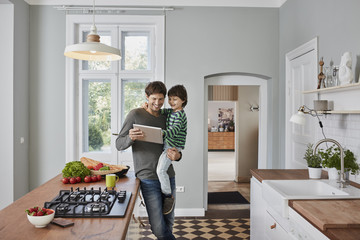 Happy father and son using tablet in kitchen together