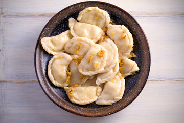 Pierogi or pyrohy, varenyky, vareniki, dumplings served with caramelized salted onion in bowl on wooden table. horizontal