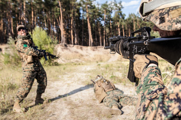 Fototapeta premium Location shot of United States Marine with rifle weapons in uniforms. Military equipment, army helmet, warpaint, smoked dirty face, tactical gloves. Military action, battlefield