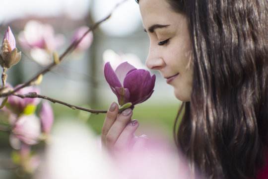 Beautiful girl smelling the flowers. Blossoming magnolia in the park garden.