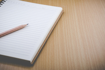 Notebook and pencil are on the wood table.