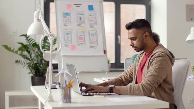 business and creative people concept - young indian man with laptop computer working at office