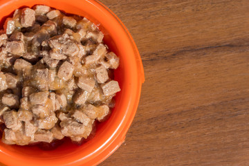 Canned food for cats or dogs in a orange plastic bowl