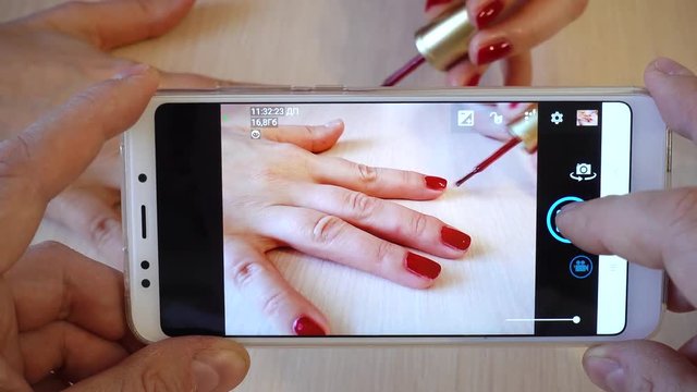One person takes a picture in the beauty salon using a modern phone. A woman in a beauty salon does a manicure, paints her nails with lacquer.