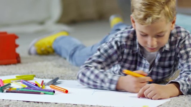 Boy of primary school age lying on the floor and drawing pictures using colored felt-tip pens