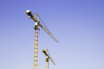 Two big yellow construction cranes on blue sky background
