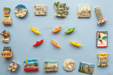  colorful paper ships and  various souvenir magnets from several world country arranged on the blue background  