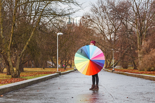 Young woman with rainbow umbrella walking outdoor in the park at a rainy day