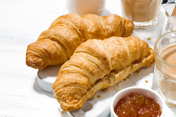 croissants with orange jam and coffee with milk on white table
