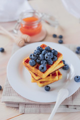 Belgian waffles with blueberries on the light wooden table. Healthy breakfast. 