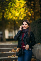 Stylish beautiful lady in a black leather jacket with a black bag and brown fur. Lady talking on the phone.