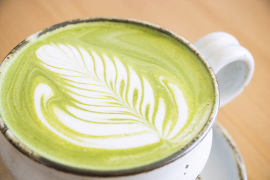 Matcha green tea latte in a cup on wooden table background.Hot Matcha coffee latte with beautiful milk foam latte art texture.