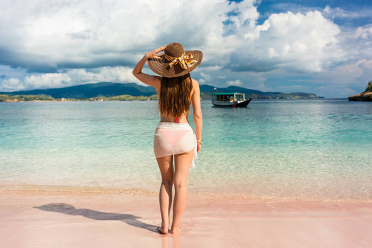 Full length rear view of an attractive young woman wearing straw hat and mesh swim skirt while looking away on the beach in Komodo Island, Indonesia