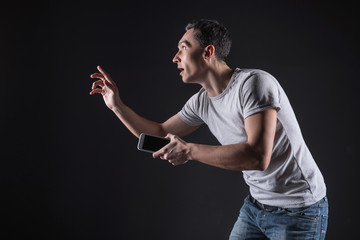 New dimension. Excited pleasant good looking man holding his mobile phone and touching the sensory screen while testing a video game