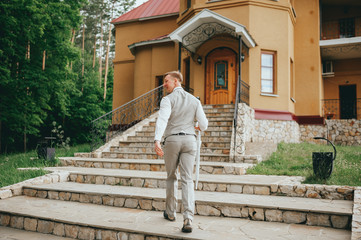 Groom in the stylish wedding suit going to the bride with a bouquet of flowers. Back view