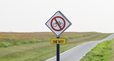 one way sign for bike lane in the park with colorful flower field at background
