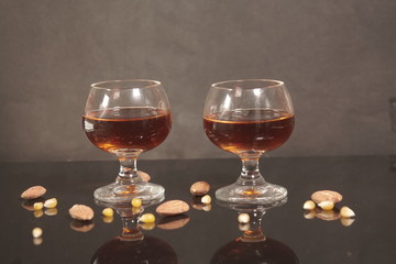 Two glass of cognac with almonds on black background.