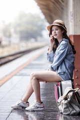 young beautiful woman is sitting on luggage and using a smartphone while waiting for a train