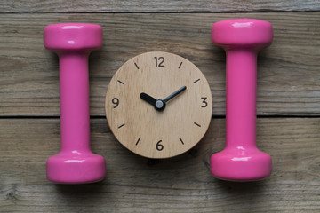 Time for exercising clock and dumbbell on table background