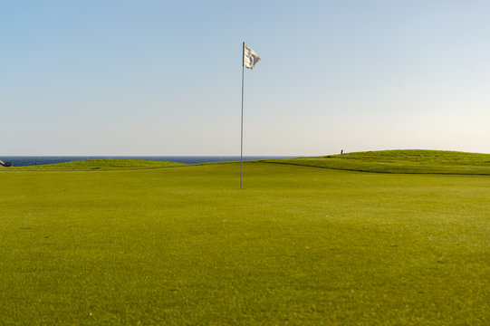 Green golf with flag and hole facing Atlantico