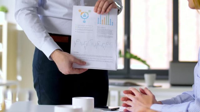 business, corporate and people concept - businessman showing papers with charts and businesswomen applauding to him at office meeting or presentation