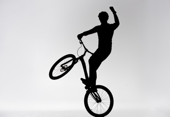 silhouette of trial biker standing on back wheel and raising hand on white