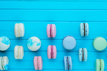 Multicolored macaroons or macarons in pastel colors lie in staggered order on a turquoise wooden background, copy space