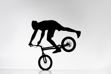 silhouette of trial biker performing front wheel balancing stunt on bicycle on white
