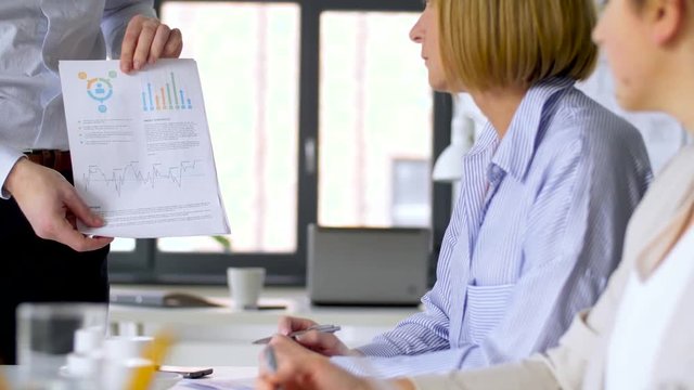 business, corporate and people concept - businessman showing papers with charts to businesswomen at office meeting or presentation