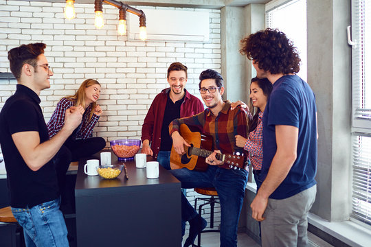A group of young people having fun playing guitar sing songs at a meeting of friends.
