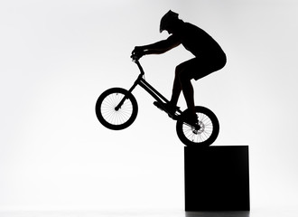 silhouette of trial cyclist performing back wheel stand while balancing on cube on white